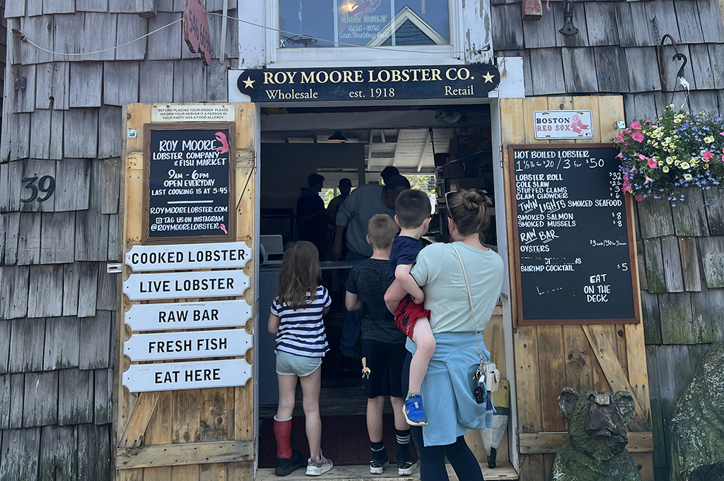 a gray shingled shack with kids and a woman standing in front of a door